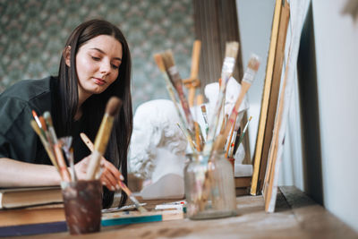 Young woman artist teenager girl student with dark long hair in casual draws picture at art studio