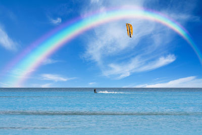 Distant man kiteboarding on sea under the rainbow