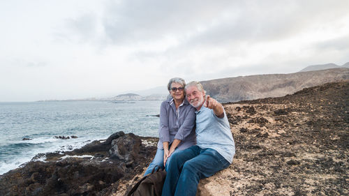 Portrait of smiling woman with man pointing by sea against cloudy sky