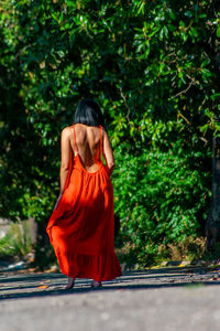 Rear view of female model standing on road against trees