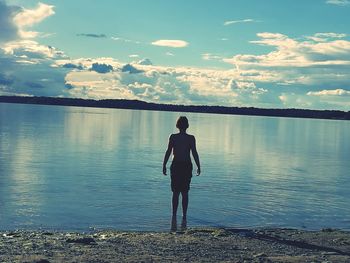 Full length of man standing in lake against sky during sunset