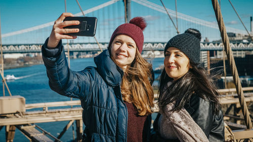 Young woman photographing while standing on mobile phone in winter