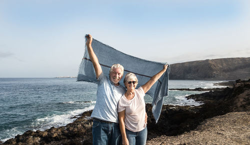 Portrait of smiling couple holding scarf while standing at beach