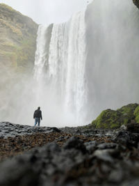 Rear view of man standing against waterfall