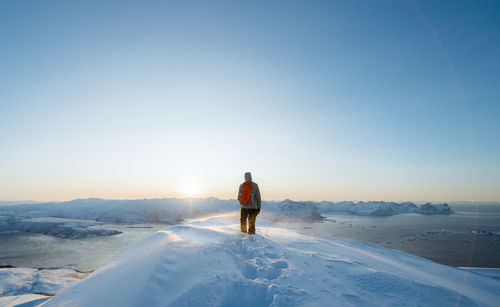 Rear view of mid adult man with backpack standing on snowcapped mountain against clear sky