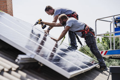 Craftsmen installing solar panels on house rooftop
