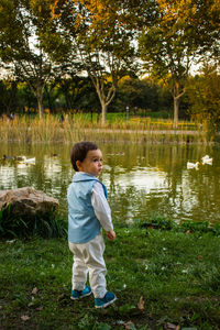 Rear view of boy standing against pond