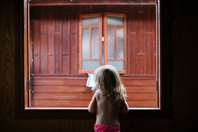 Rear view of young girl looking through window