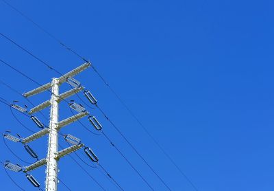 Low angle view of electricity pylon against clear blue sky