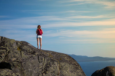 Rear view of woman standing on rock by sea against sky