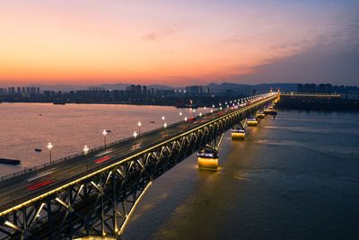 Illuminated bridge over river against sky at sunset