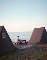 Rear view of man sitting on seat in sea against sky