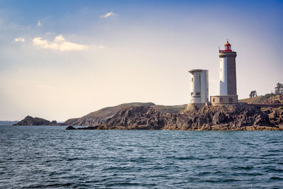 Lighthouse by sea against sky during sunset