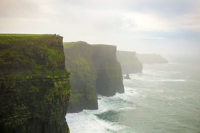 Scenic view of sea by cliff against sky during foggy weather