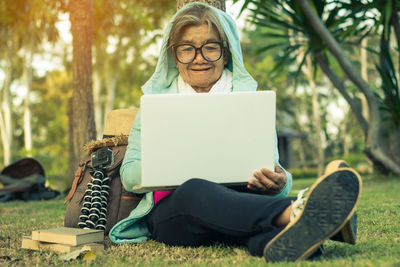 Senior woman using laptop while sitting on grassy field in park