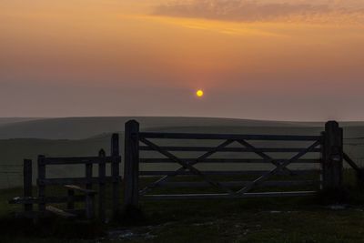 Silhouette fence against sky at sunset