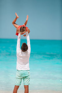 Rear view of father holding daughter mid air against sea