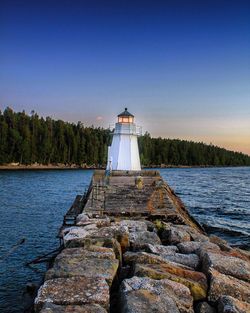 Lighthouse by lake against clear blue sky