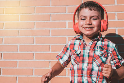 Cheerful boy listening music while standing against wall