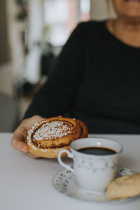 Hand holding cinnamon bun, coffee on foreground