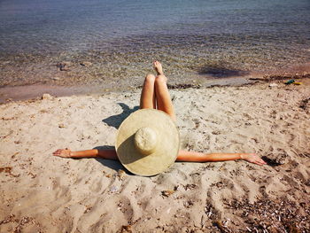 Mature woman lying on a sand beach her head covered with hat