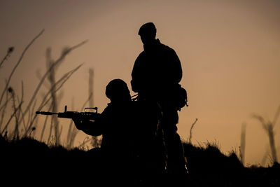 Silhouette hunters on field against sky during sunset