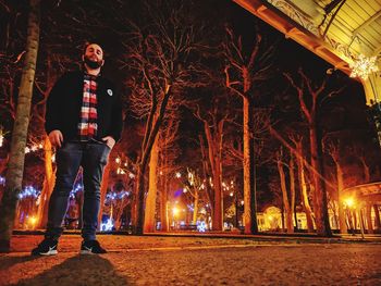 Low angle view of man standing by illuminated trees at night