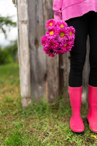 A girl in pink boots stands against the background of an old house and holds a bouquet of flowers.