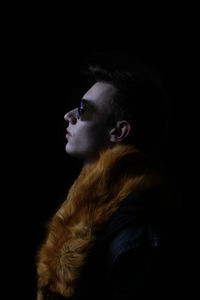 Close-up of man wearing fur collar against black background