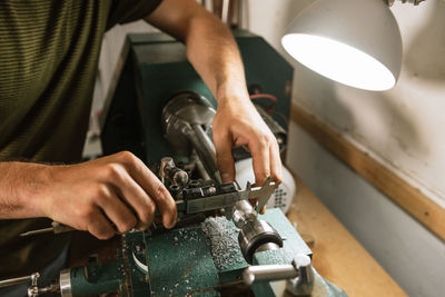 Unrecognizable technician standing at workbench and using caliper for precise gauging while working in shabby workshop
