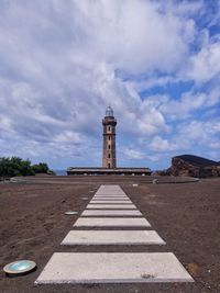 View of lighthouse by building against cloudy sky