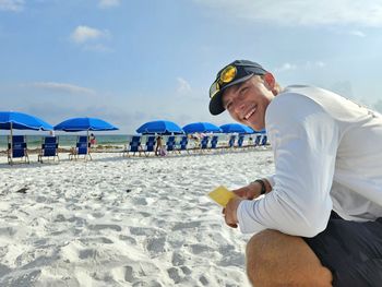 Smiling millennial man setting up beach chairs in summertime for tourists on vacation.