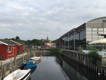 Boats moored in canal amidst buildings in city against sky