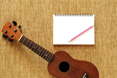 Directly above shot of guitar with pencil and spiral notebook on textile