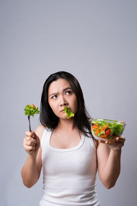 Portrait of young woman holding food against white background