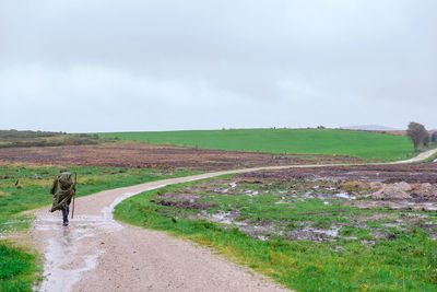 Person walking on dirt road against sky