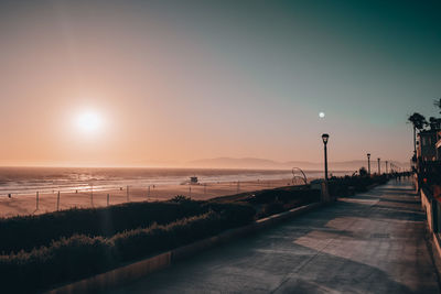 Street by sea against sky during sunset