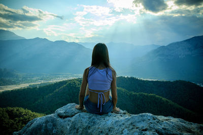 Rear view of man sitting on rock against mountains