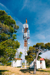 Low angle view of communications tower and tree against sky