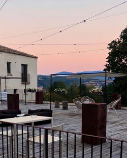 Chairs and table by buildings against sky during sunset