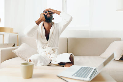 Rear view of woman using mobile phone while sitting on bed at home