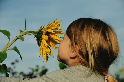 Close-up of girl smelling sunflower against sky at park