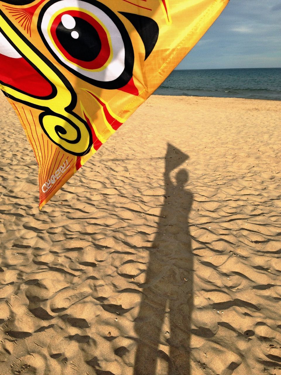 beach, sea, sand, shore, horizon over water, shadow, sunlight, sky, water, flag, yellow, outdoors, tranquility, day, identity, vacations, travel, nature, beach umbrella, high angle view