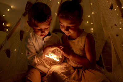 Sibling holding light while sitting in room during christmas