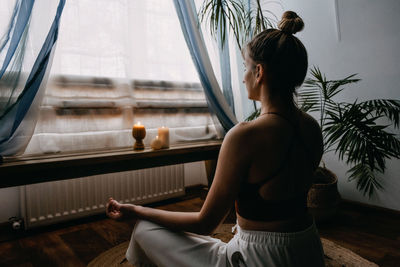 Rear view of woman sitting by window at home