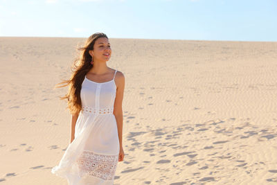 Smiling young woman looking away while standing on sand at desert