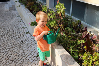 Portrait of a blond boy with a watering can. a four-year-old boy smiles and waters flowers. 