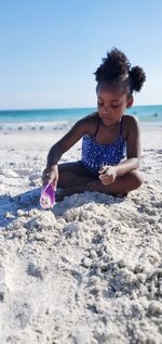 Full length of girl playing with sand at beach against clear sky