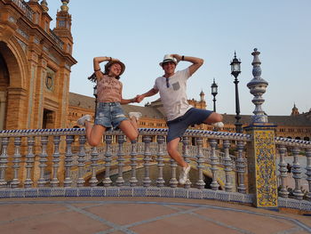 Full length of happy excited friends jumping against buildings in city