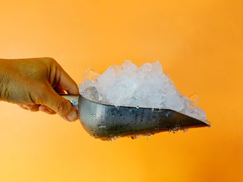 Close-up of hand holding ice cream against orange background